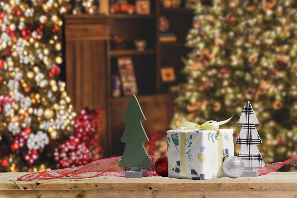 Decorative Christmas scene with gift, trees, and ornaments on a wooden table.